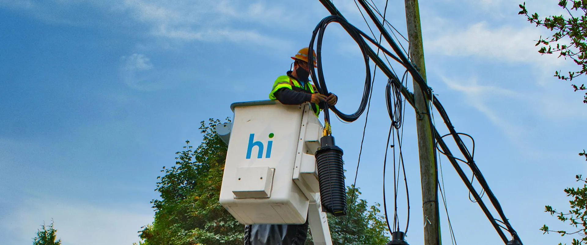 Ziply Fiber worker wearing a hardhat in the raised bucket of a construction crane 