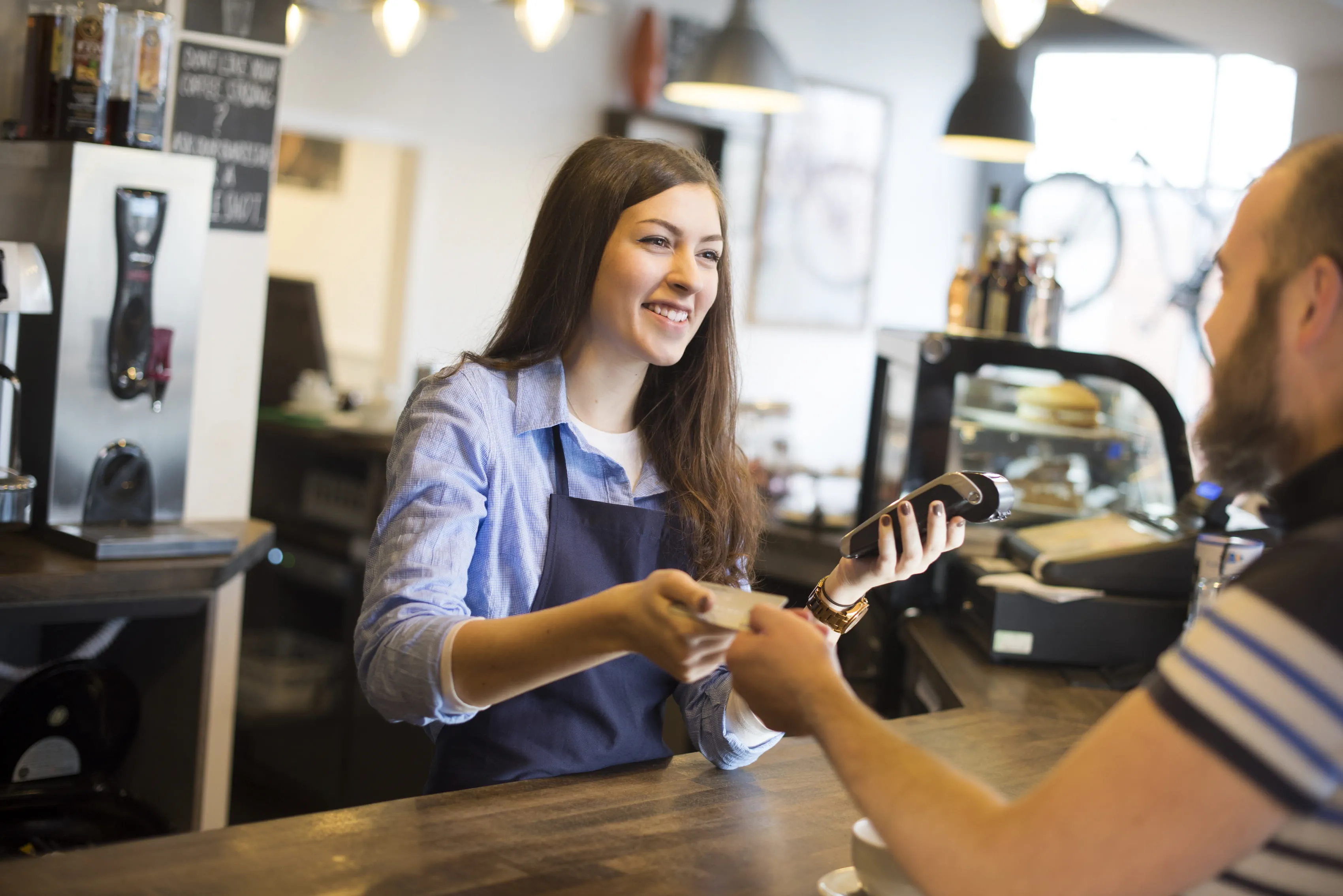 Barista holding WiFi connected payment device and smiling at a customer