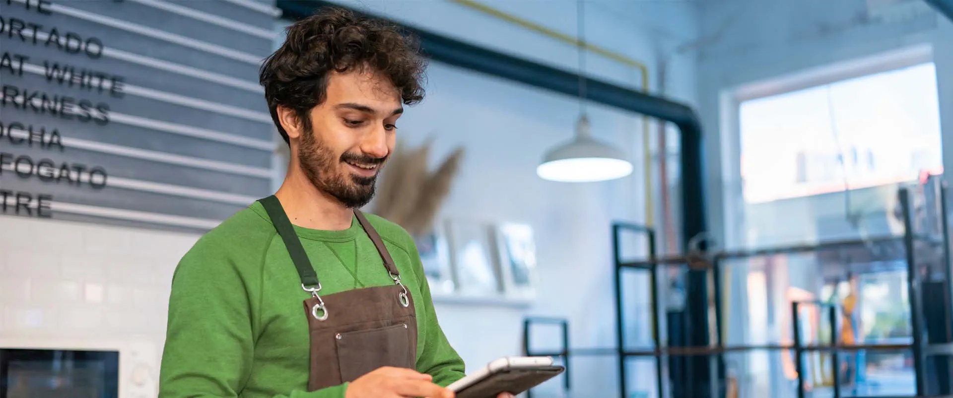 one person wearing an apron and holding a tablet in a cafe